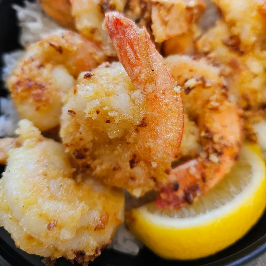 Close-up of crispy garlic shrimp with lemon wedges, served over rice, showcasing a classic Kahuku Style Garlic Shrimp by Pua's Plate Lunch catering.