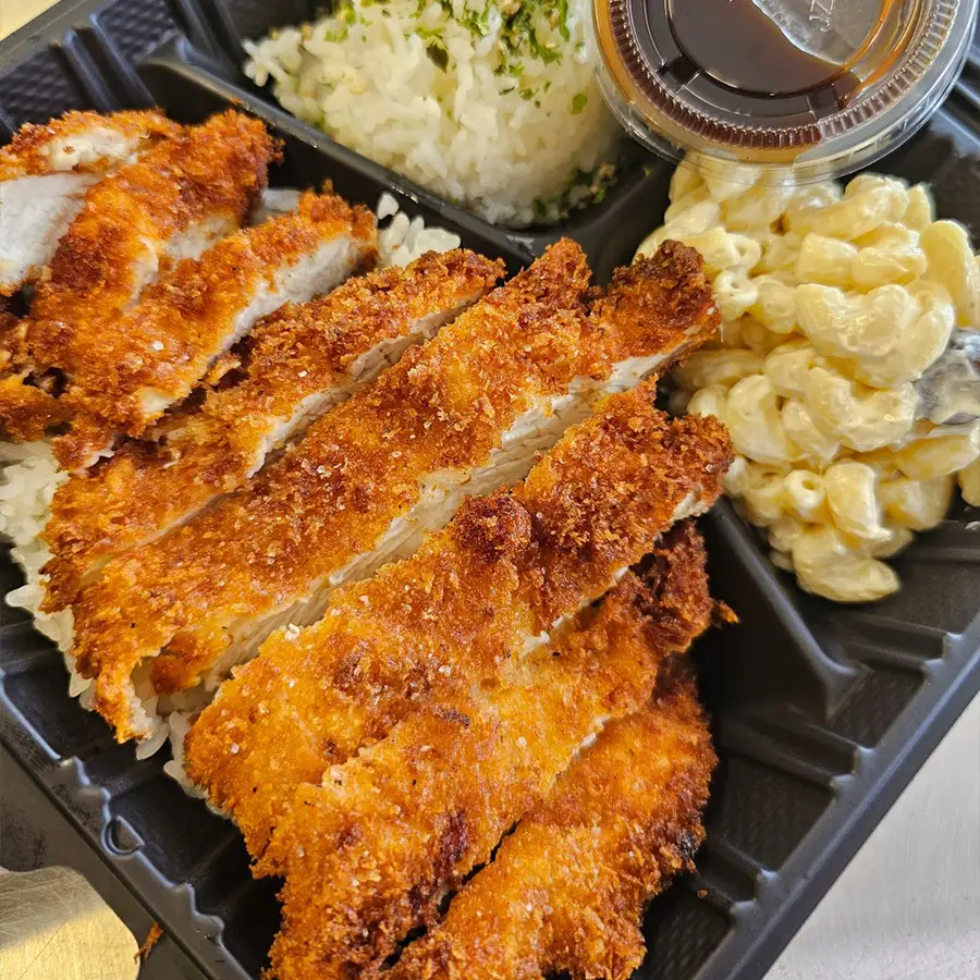 Crispy chicken katsu with rice, macaroni salad, and sauce in a black bento box, showcasing Hawaiian cuisine from Pua's Plate Lunch.