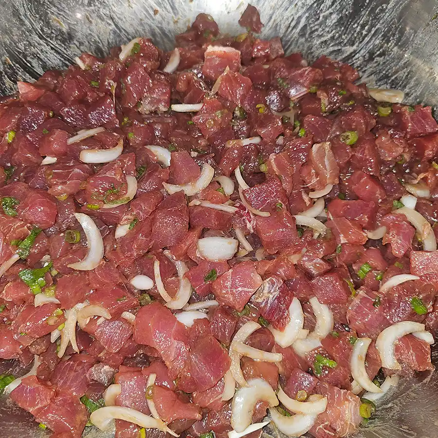 Fresh ahi poke with diced fish, onions, and herbs in a metal bowl, showcasing Hawaiian cuisine from Pua's Plate Lunch catering.